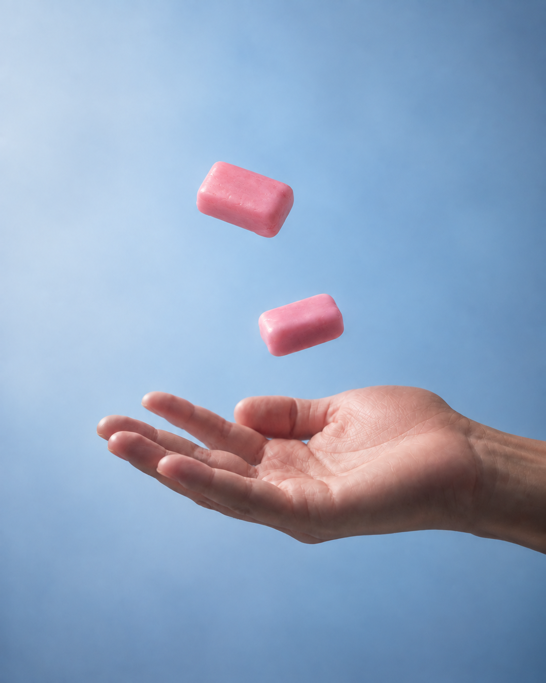 Two unwrapped strawberry-pink soft chews floating above an open hand in pale-blue light